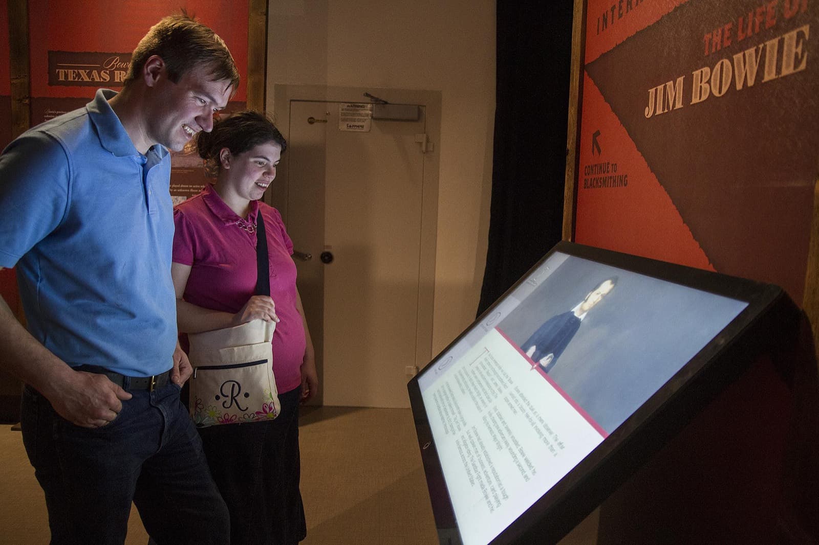Two visitors reading an interactive kiosk beside the Life of Jim Bowie entrance graphics.