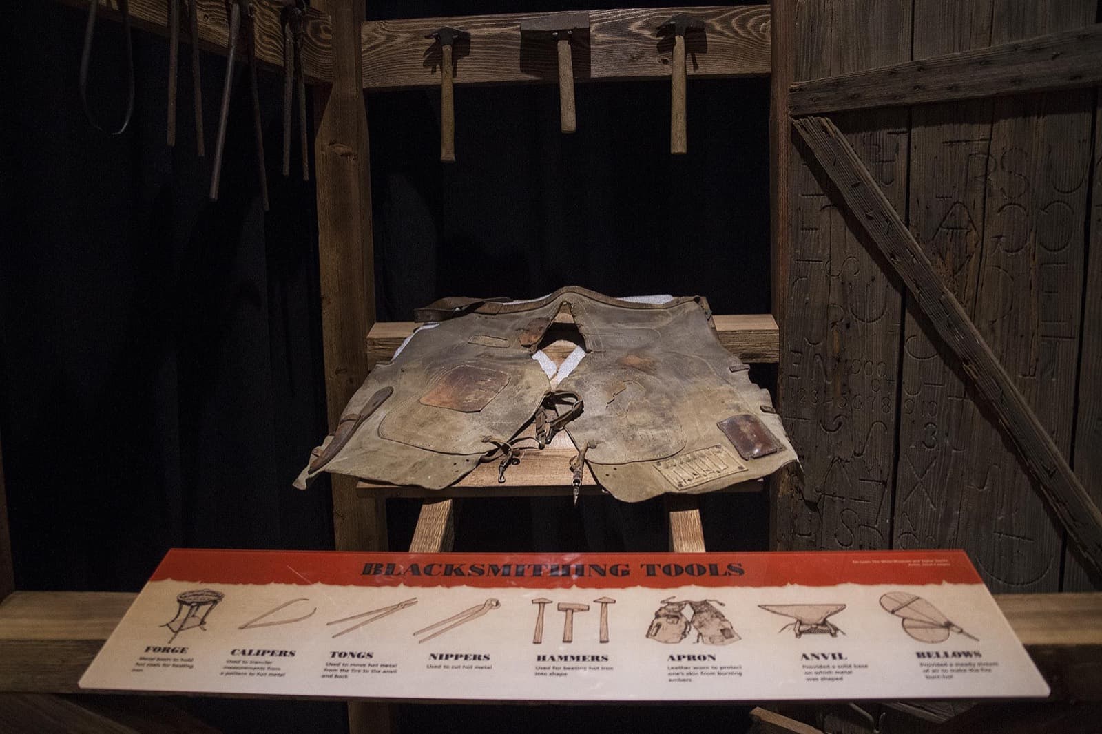 A blacksmith's leather apron and tools displayed with an illustrated identification panel.